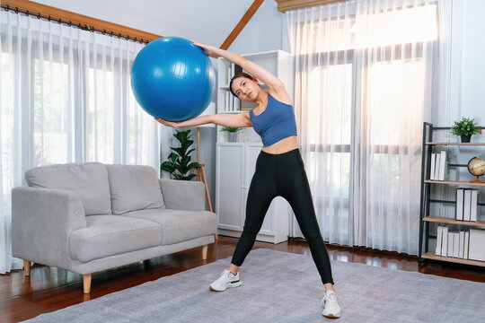 Young attractive asian woman in sportswear hold and lift fit ball targeting on abs muscle for effective energetic home exercise routine. Vigorous