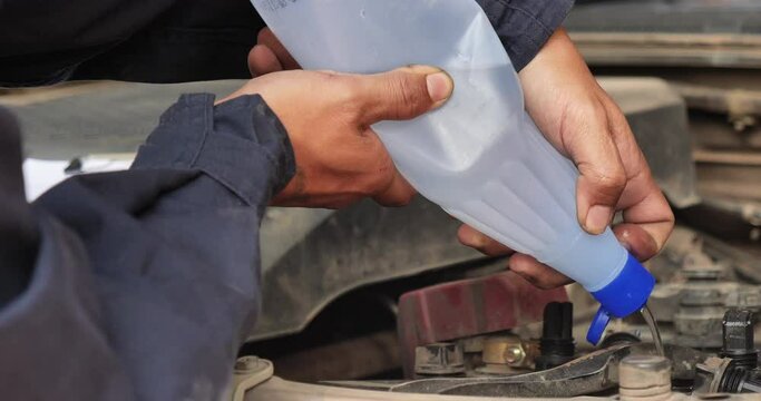 Car Mechanic man hands pouring Deionized purified Distilled water for car battery mechanical service. Close up hands man hold Deionized Distilled liquid water bottle at garage auto mobile car service