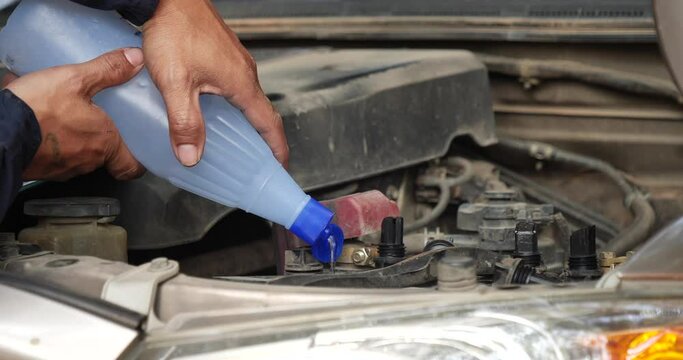 Car Mechanic man hands pouring Deionized purified Distilled water for car battery mechanical service. Close up hands man hold Deionized Distilled liquid water bottle at garage auto mobile car service