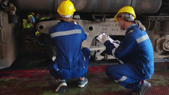 Young caucasian engineer man and woman maintenance and repair train diesel engine in station, team engineer inspect system transport, technician checking infrastructure, transportation and industry.