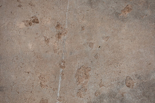 Detail of a deteriorating concrete floor with cracks and pock marks. The concrete has a brown-beige color with hints of grey.