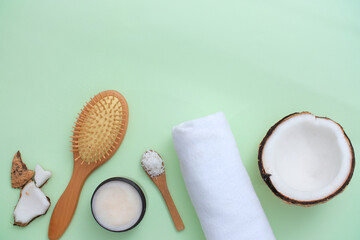A detangling comb, wooden spoon, cloth towel, ceramic plate and fresh coconut are arranged at the bottom of the frame. Creative space for advertising shower gel, shampoo and more.