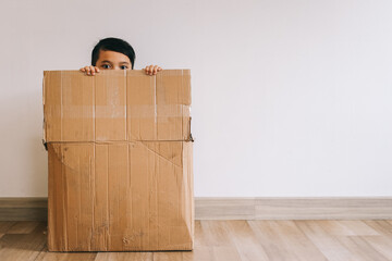 Little Asian boy hiding inside cardboard box - obrazy, fototapety, plakaty