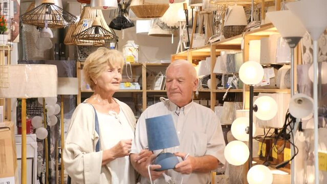 Portrait of mature couple choosing table lamp at store of household goods. High quality 4k footage