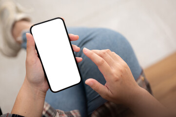 A woman using her smartphone while sitting indoors. A smartphone blank screen mockup