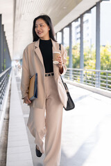 A confident Asian businesswoman is walking on the skywalk in the city with her stuff.