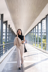 A busy and confident Asian businesswoman is talking on the phone while walking on a skywalk.