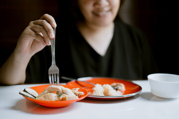 Young Asian girl is forking a piece of chicken with smile face expression bokeh background