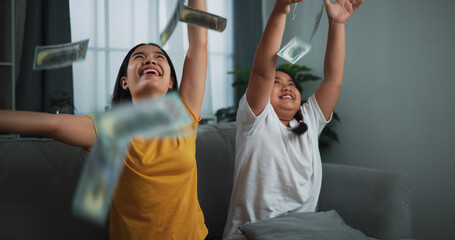 Portrait of a young woman and teenage girl enjoying scattering cash bills on a sofa in the living room at home.