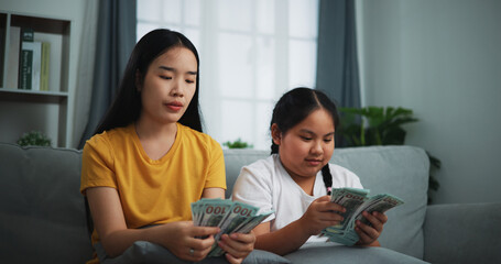 Portrait of young women and teen girl counting cash money on sofa in the living room at home,Happy counting dollars banknote.