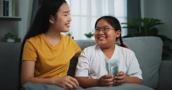 Portrait Of Young Woman Giving Dollars Money With Teen Girl For Doing Great Work At Home.