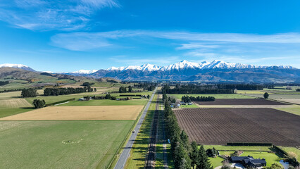 Aerial farming grazing and crop fields in rural  countryside with a backdrop of the snow capped Mountain range under clear skies