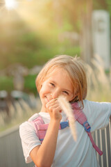 A little girl smiles and holds a blade of grass in her mouth. Portrait of a 6-year-old child with blond hair close-up on the street