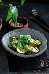 Grilled zucchini with pesto sauce. Vegetable dish with chopped zucchini in a gray plate served with basil, on dark background