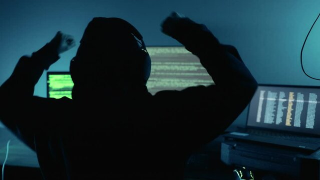 Professional hacker successfully using code login breaks into company data servers and raised hands celebrating in dark atmosphere. Cyber crime, Digital system security