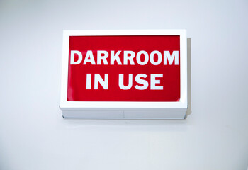 Vintage box shaped sign on a wall stating Darkroom In Use with white letters on a red background