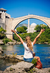 Fototapeta na wymiar Female tourist looking at famous old bridge and river of Mostar- tour tourism,travel,vacation in Bosnia