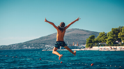 Young boy, happy child jumping in the air on the beach, into the sea- vacation, happiness, travel destination concept