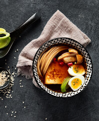 Asian soup with egg, tofu, mushrooms and onion on black background. Traditional food concept.