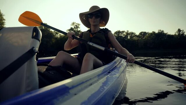 woman wearing hat kayaking on lake during sunset and holding an oar