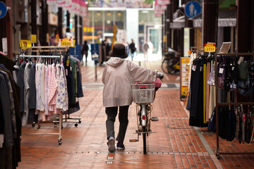 朝の商店街で自転車を押して歩く一人のシニア女性の姿