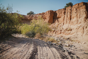 Sandy wash with tire tracks next to red dirt banked wall in Camp Verde Arizona on sunny day