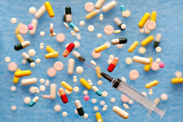 Pills, capsules with medicines and a disposable syringe on a blue background, there is space for copy.