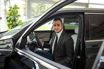 Cheerful man client holding key sitting inside new auto at dealership