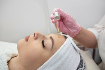 closeup of beauticians hands is putting few drops essential oil with a pipette on the face women