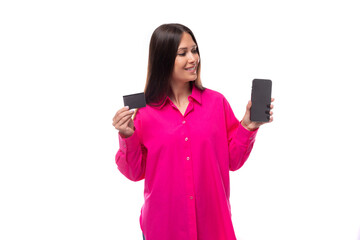 smiling brunette european woman in crimson shirt holding credit card and smartphone mockup