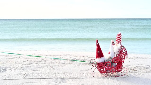 Christmas Gnome on the beach in a red sled on a sunny winter day