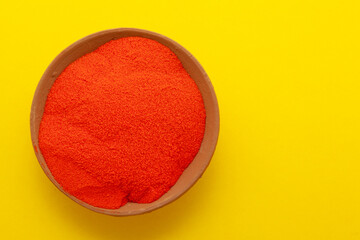 Top view of orange color traditional Rangoli powder in clay lamp isolated on a yellow background.