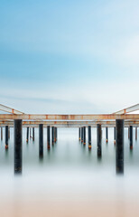 Fine art view of columns under metal pier at sunrise. Shot with long exposure to make the sea appear as fog