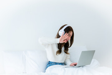 Morning Time in Bedroom Young Asian Woman Happy Working on Computer Laptop, Wearing headset, Sitting on Bed at House