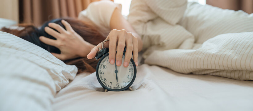 alarm clock and asian woman hand stop time in bed while sleeping, young adult female wake up late in the early morning. Relaxing , sleepy, daily routine and have a nice day concepts