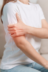 Woman having arm pain during sitting on couch at home, muscle injury and ache. Health and medical concept