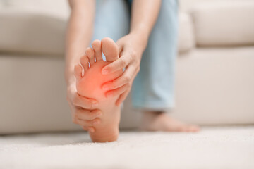 woman having barefoot pain during sitting on couch at home. Foot ache due to Plantar fasciitis and waking longtime. Health and medical concept - obrazy, fototapety, plakaty