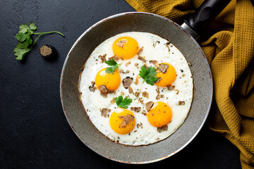 Fried eggs with black truffle in a pan. Top view. Italian food. Dark table surface.