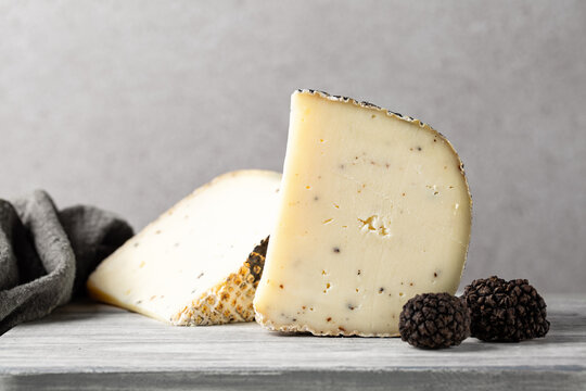 Aged sheep's milk pecorino cheese with black truffles flakes. Fresh whole truffles on a board. Italian luxury products.