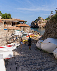 Tourists stroll through the beautiful old streets of the small coastal village of Deia in Mallorca, Spain. Traditional houses terraced on the hills, white boats lined up on the shore.