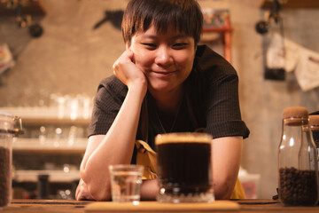 A Happy and smart female or LQBTQ coffee shop entrepreneur or barista is wearing apron stand with inspiration while looking at a coffee that she made with heart. Work life balance Startup SME business