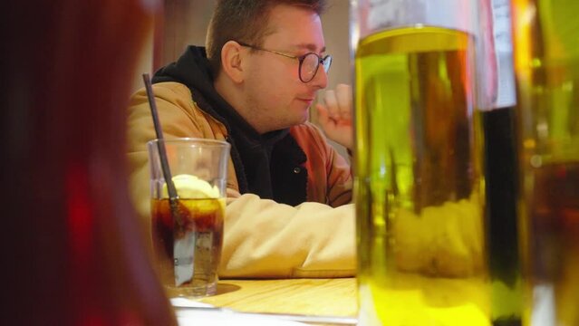 Young adult male sitting down in bar surrounded by alcohol and chatting