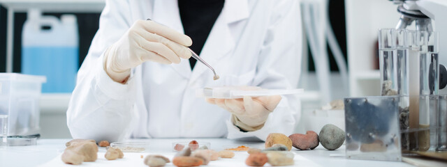 Close up of geologist or archaeologist is picking and focusing on a sample of rock, stone or mineral in paleontology, archaeological and geological or mining laboratory. Concept of ground research. - obrazy, fototapety, plakaty