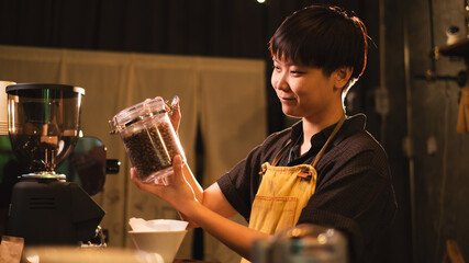 Female Barista is holding a jar of coffee beans and test the smell in loft coffee shop, cafe bar....