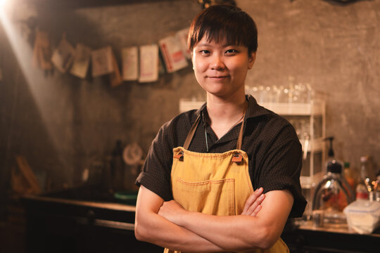 A confidence, prouded and smart female or LQBTQ coffee shop entrepreneur or barista is wearing apron stand with inspiration. Work life balance. Startup SME business. Happiness while working with job.