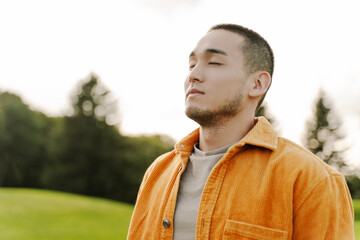 Portrait of handsome young Asian man with closed eyes wearing stylish casual clothes, yellow shirt
