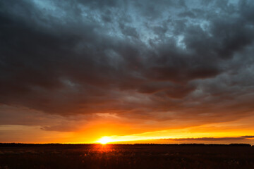 Sunset above forest and agricultural field in autumn time, yellow orange color sunset, low key photo