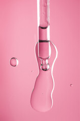 Cosmetic dropper with serum, beauty cosmetics dripping, on pink background. Macro shot. Serum, peptides, beauty and health care products. Glass pipette with liquid, close up. Top view. Skin care