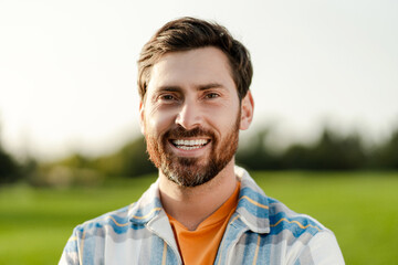 Positive bearded man farmer standing in field, outdoors, looking at camera. Advertisement concept