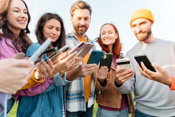 Smiling stylish friends wearing casual clothes holding mobile phones using mobile app in park